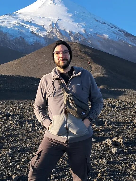 Jorge Araya standing on volcanic rock below the snow-capped Osorno Volcano in Chile